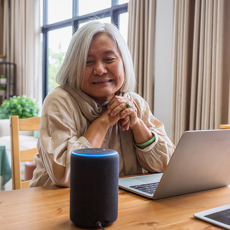 Asian eldery woman sitting on a desk and watching Alexa speaker